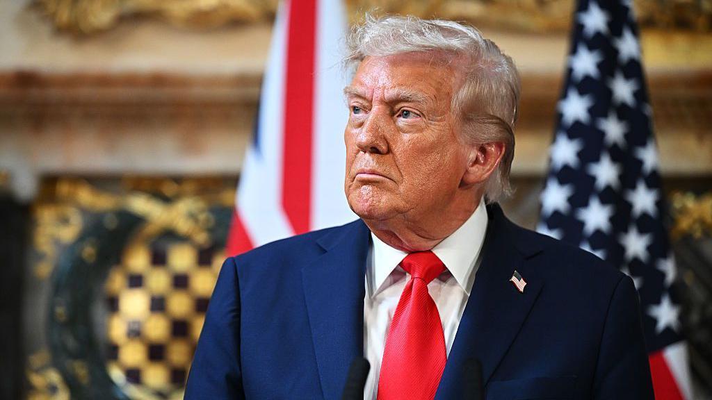 Donald Trump, con traje azul marino y corbata roja, mira de lado con gesto serio