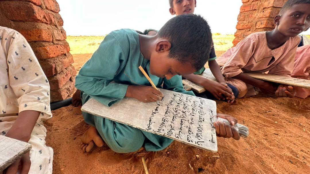 أربعة أطفال يتعلمون الكتابة في مدرسة نصبت في الساحة.