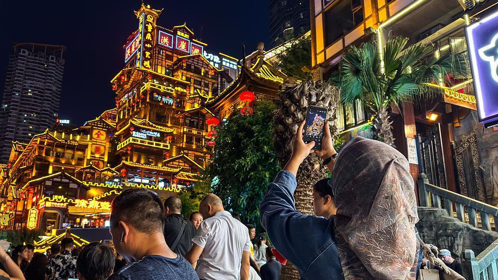 una persona toma fotos a un edificio repleto de luces en Chongqing