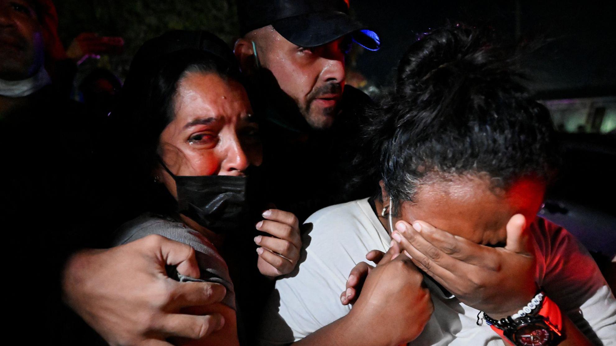 Un grupo de familiares y amistades reaccionan durante un operativo de rescate en La Guaira, Venezuela. Un hombre abraza a una mujer visiblemente conmocionada y otra se cubre la cara con la mano llorando. 27 de junio 2026