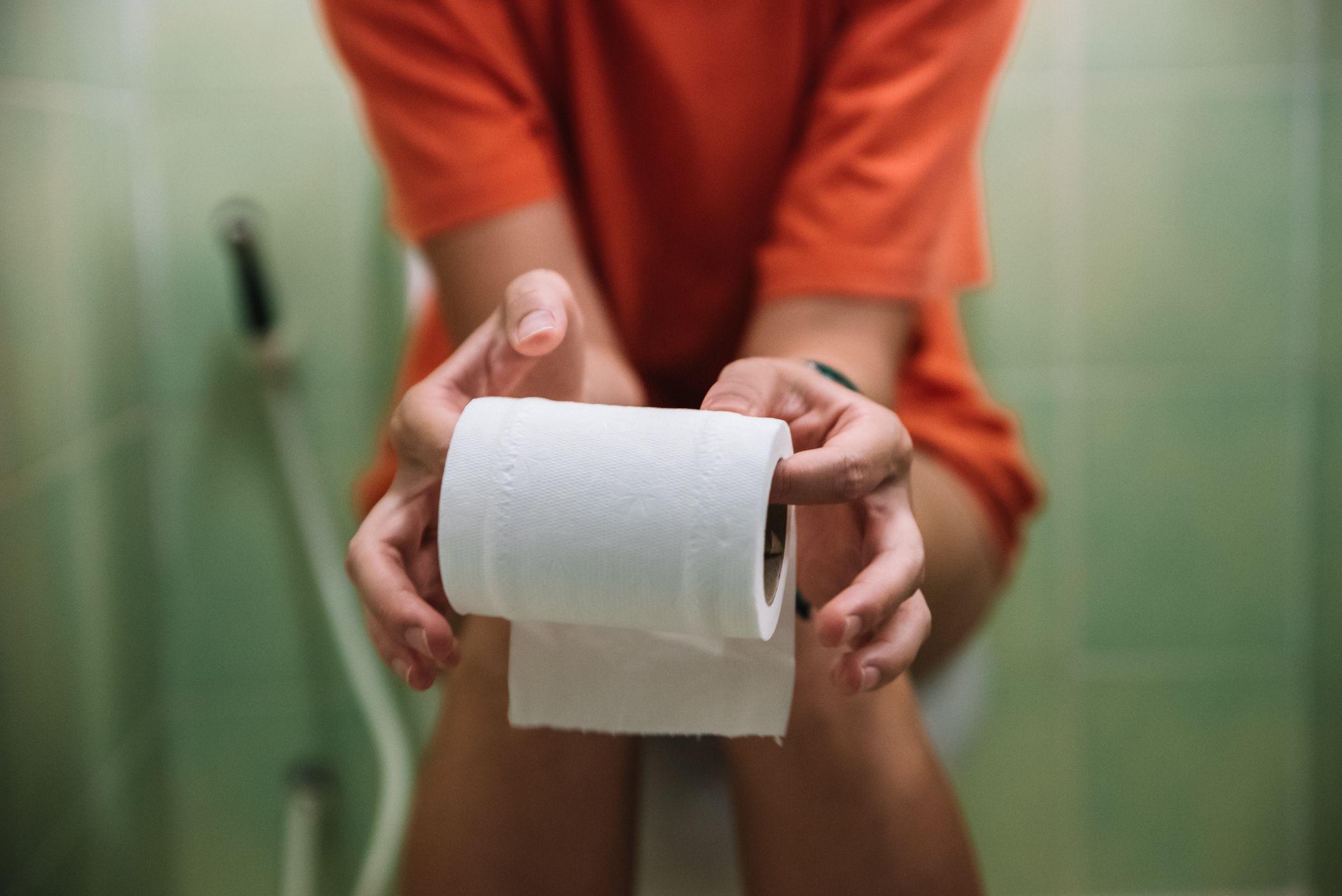 Una mujer sentada en un inodoro con un rollo de papel en los dedos