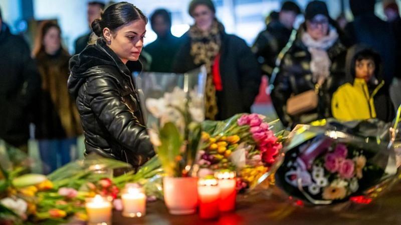 Una mujer observa las flores y velas depositadas en homenaje a las víctimas del incendio del 1 de enero de 2026 en Suiza y se ven otras personas de fondo
