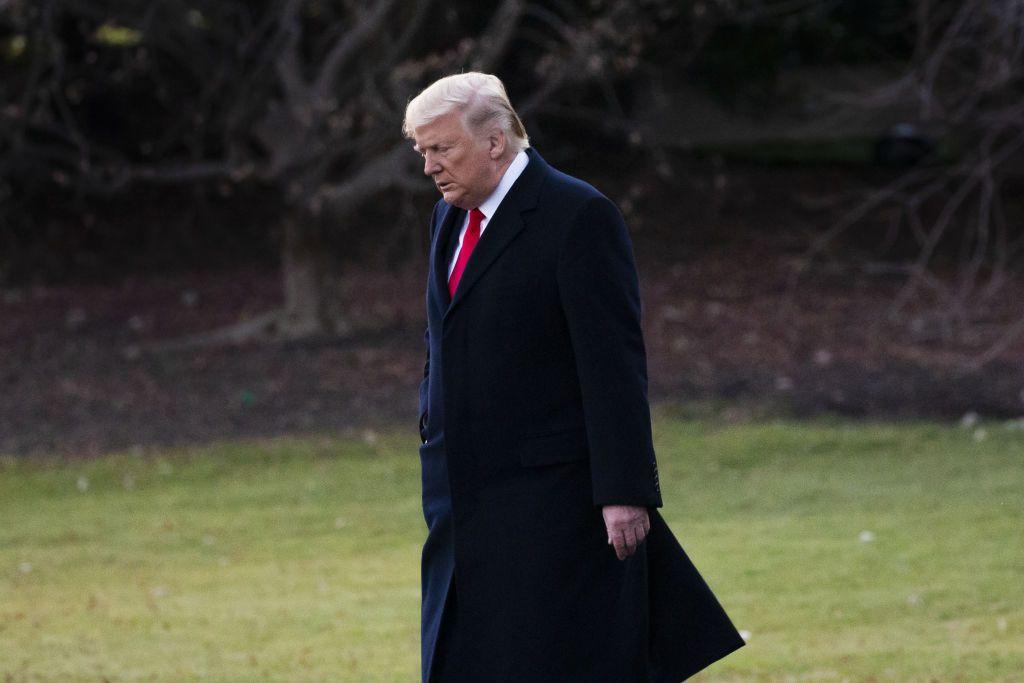 Donald Trump, recién bajado del helicóptero presidencial, con un gran gaván negro y una corbata roja, camina con la mirada al suelo.