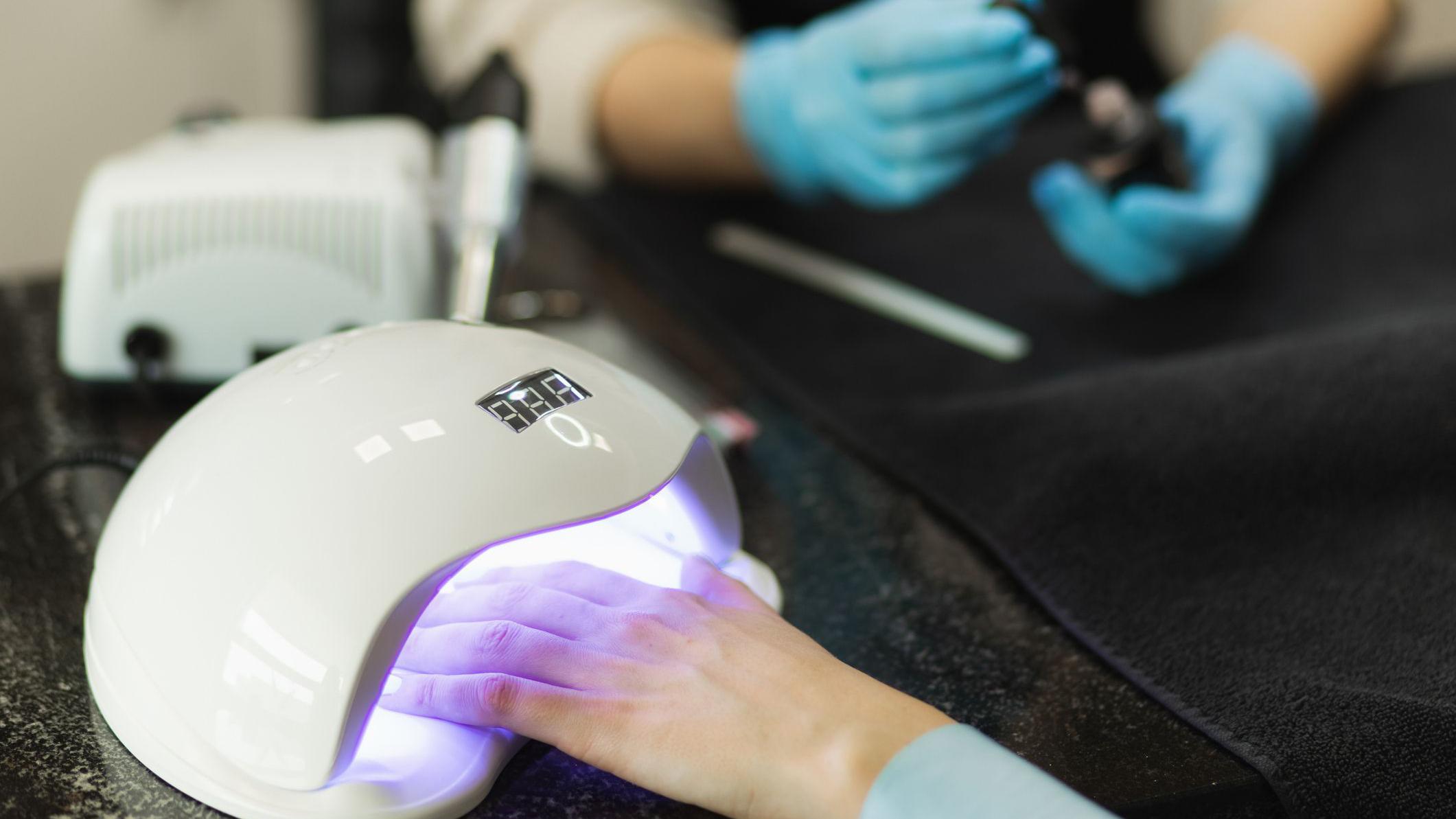 خبيرة تجميل أظافر تغطي أظافر يدي إحدى الزبونات التي وضعت طلاء أظافر "الجل" لتجفيف الطبقة العليا في جهاز تحت ضوء الأشعة فوق البنفسجية.