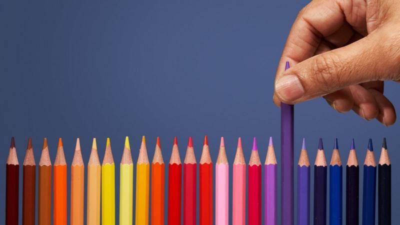 Uma m&atilde;o pegando um l&aacute;pis de cor em uma fileira de l&aacute;pis coloridos 