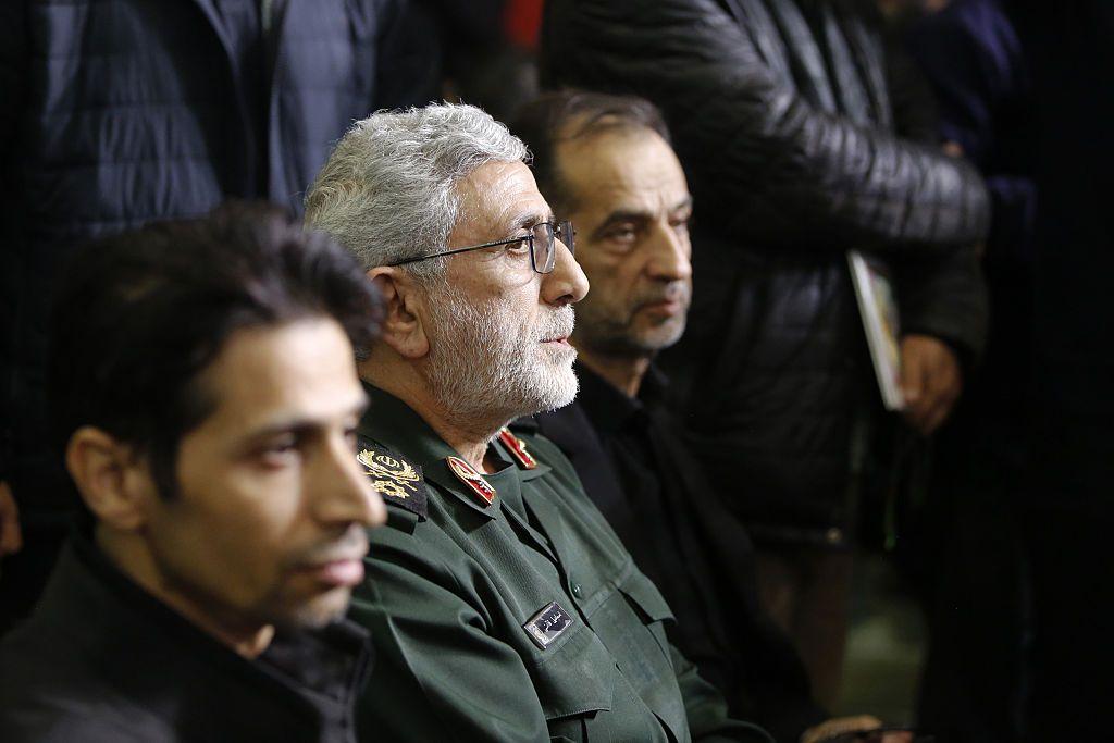 يجلس العميد إسماعيل قاآني متجهاً نحو اليمين، بين رجلين آخرين، بينما يضيء شعاع من الضوء وجهه، في حفل تأبين أقيم في 17 فبراير/شباط 2026.
