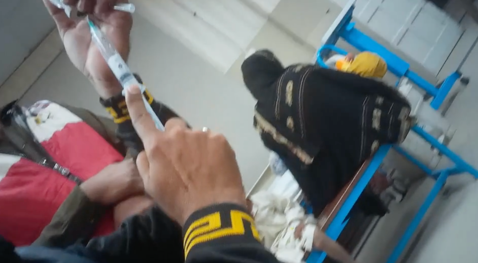 تصوير سري يُظهر متطوعاً في مستشفى يعيد استخدام حقنة بعد حقن طفل، ما قد يؤدي إلى تلوث الدواء.