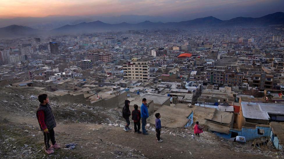 Niños en la ladera de una colina mirando hacia el valle donde está Kabul rodeada de montañas