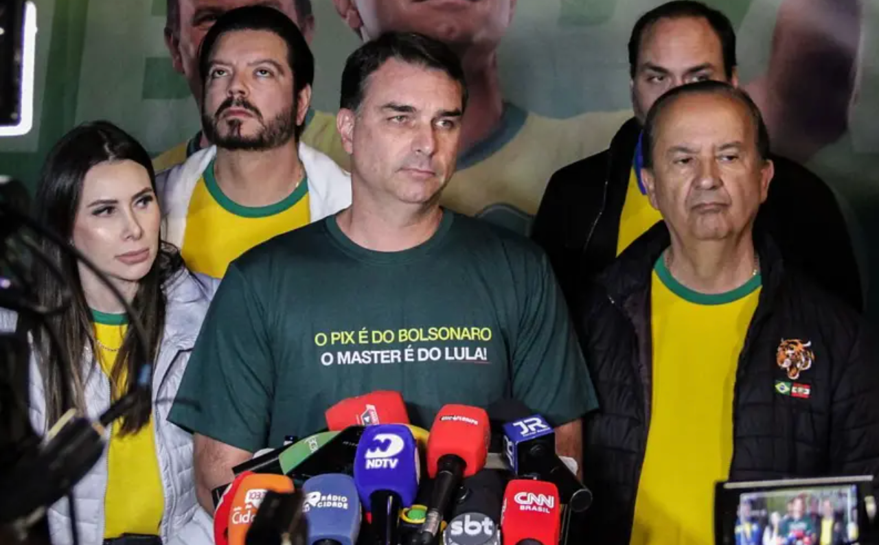 Fl&aacute;vio Bolsonaro cercado por apoiadores usando camisas amarelas enquanto Fl&aacute;vio usa uma verde escrito: 