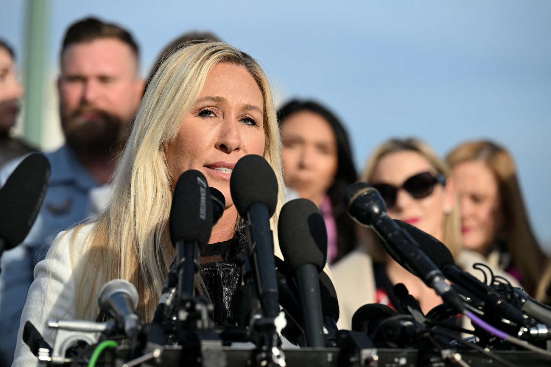 Marjorie Taylor Greene fala em uma conferência de imprensa ao ar livre. Vários microfones grandes estão agrupados na frente dela.