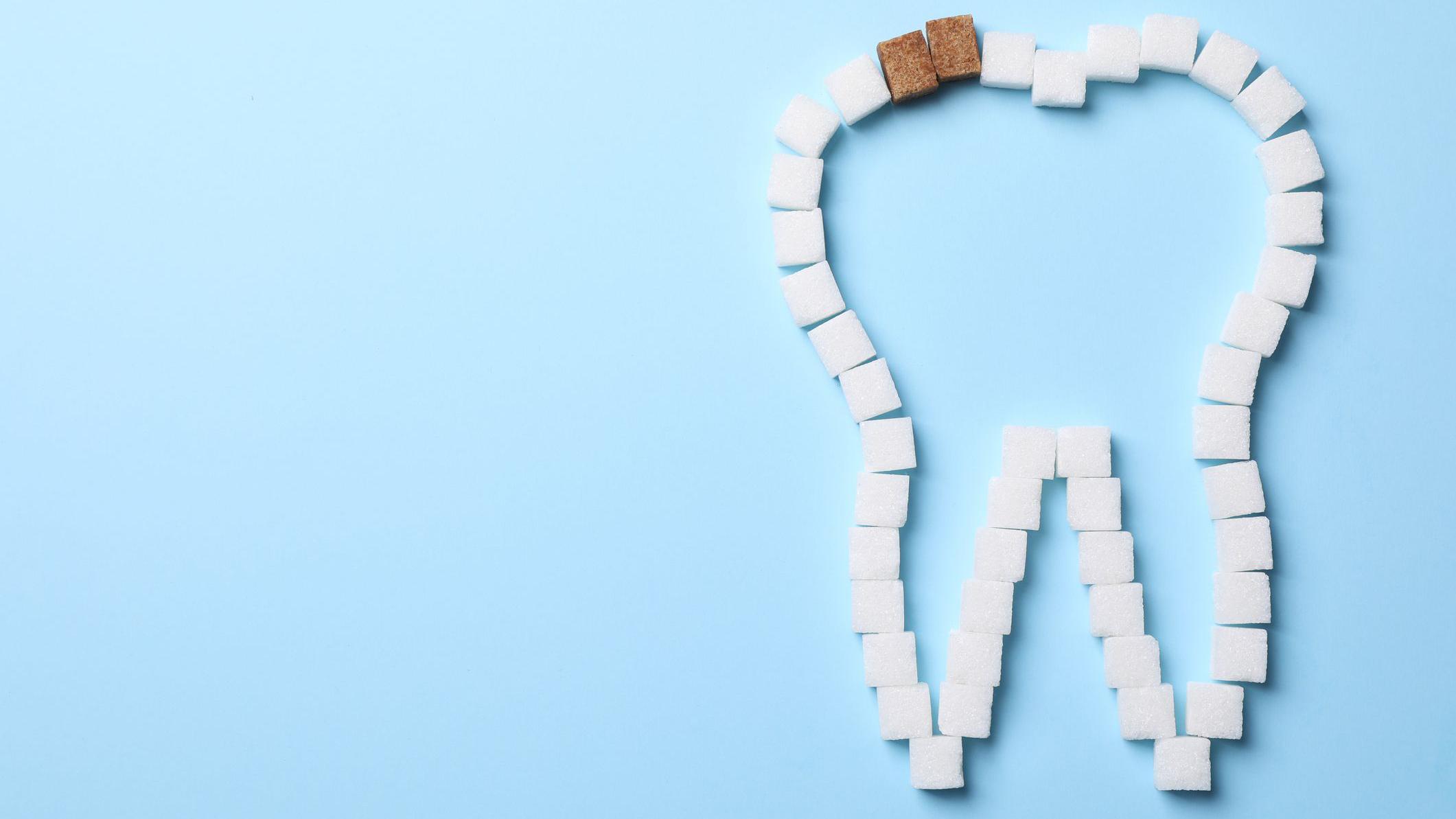 ilustración de varios cubos de azúcar que forman un diente. Dos de los cubitos son color marrón, mientras el resto son blancos. 