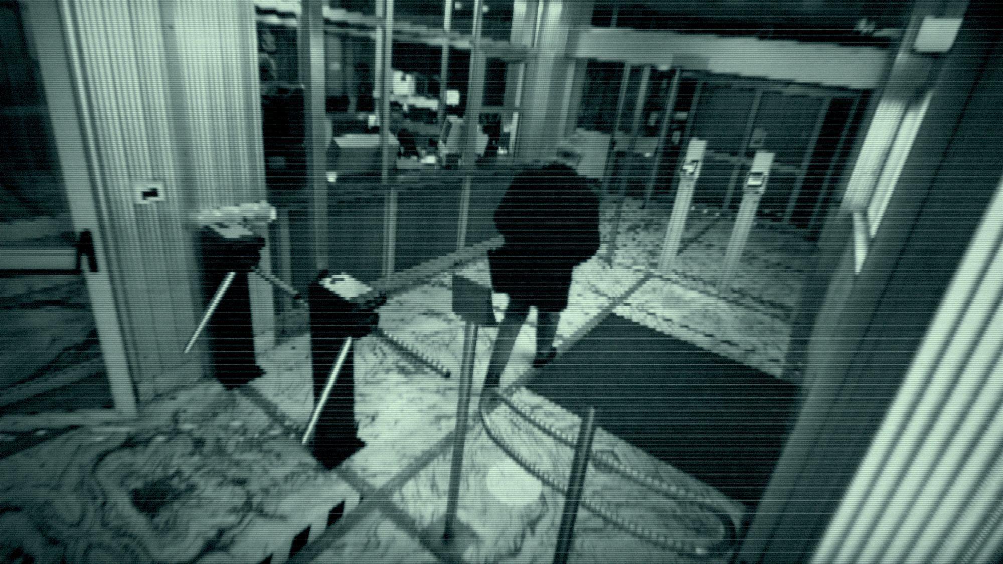 Imagen de cámara de seguridad mostrando a una persona entrando por torniquetes en un vestíbulo con suelo de mármol y puertas de vidrio