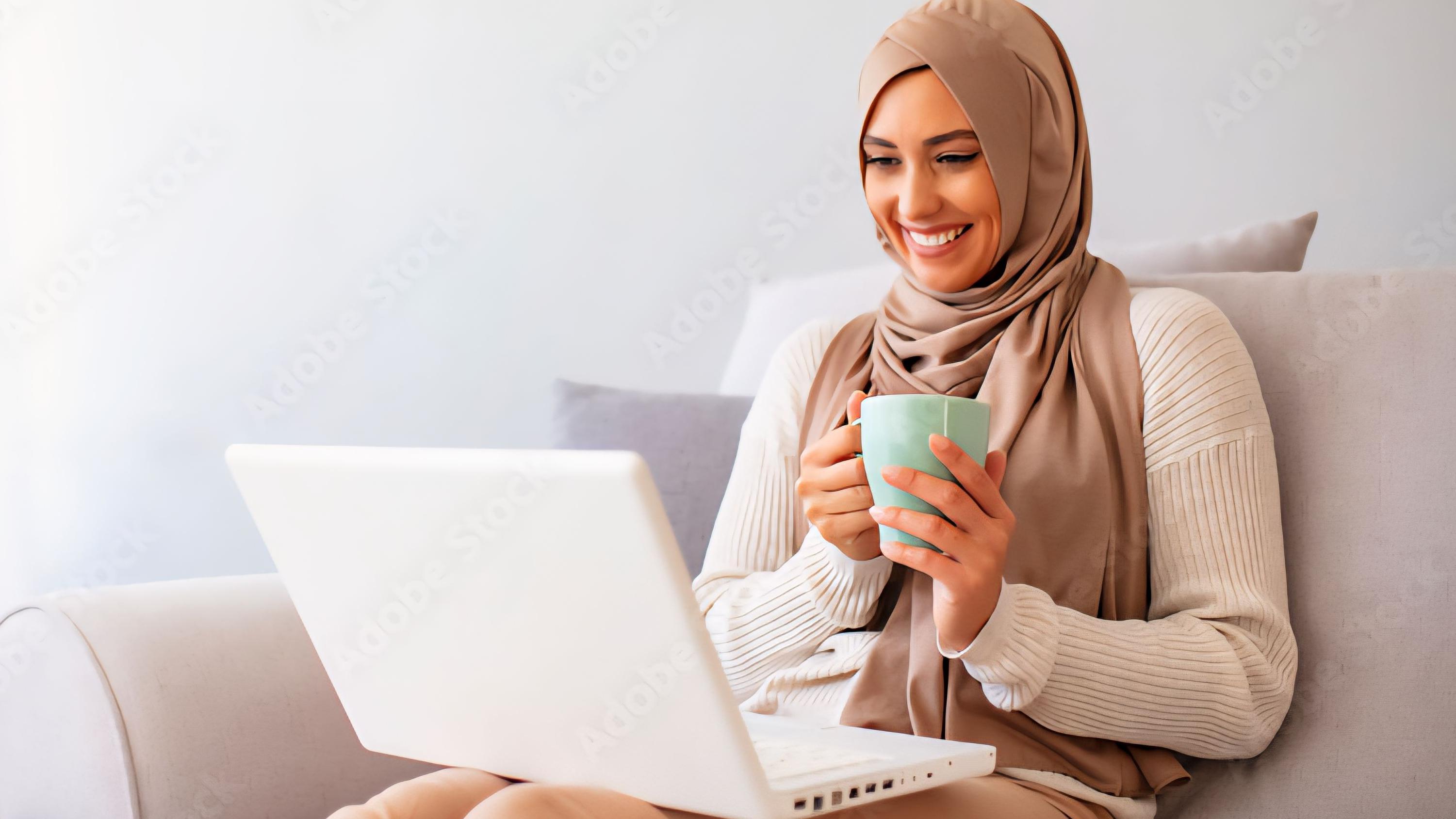 شابة محجبة تبتسم لشاشة كمبيوتر محمول