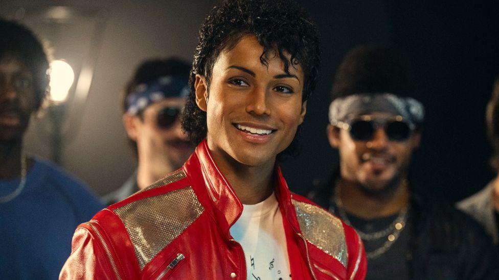 Jaafar Jackson interpretando a Michael Jackson en la película biográfica musical "Michael", luciendo una chaqueta roja y plateada.
