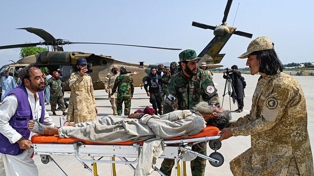 Voluntarios afganos y personal de seguridad talibán transportan a una víctima del terremoto evacuada por un helicóptero militar desde el distrito de Nurgal de la provincia de Kunar