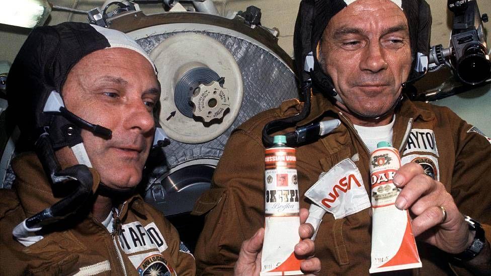 Los astronautas Thomas P. Stafford y Donald K. Slayton sostienen recipientes con comida espacial soviética