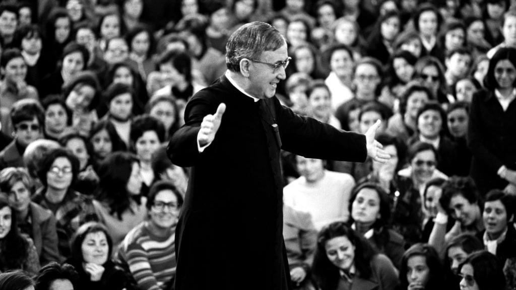 Josemaria Escriva de Balaguer em p&eacute;, sorrindo e erguendo os bra&ccedil;os, observado por multid&atilde;o