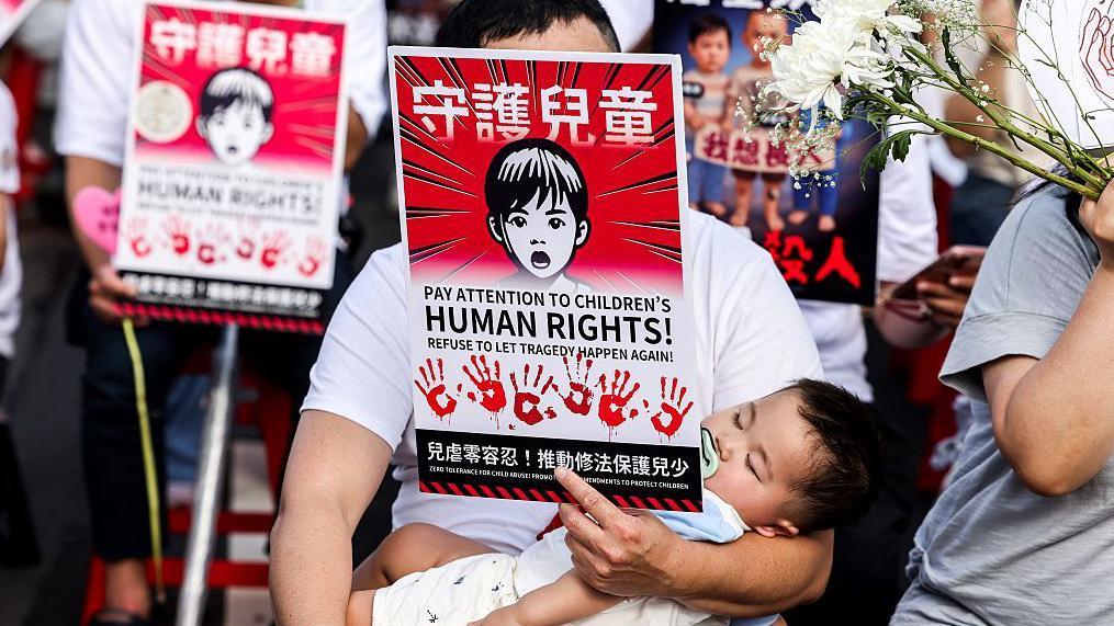 台灣一名男子帶著孩子，上街參與集會，訴求台灣政府正視兒少受虐問題。