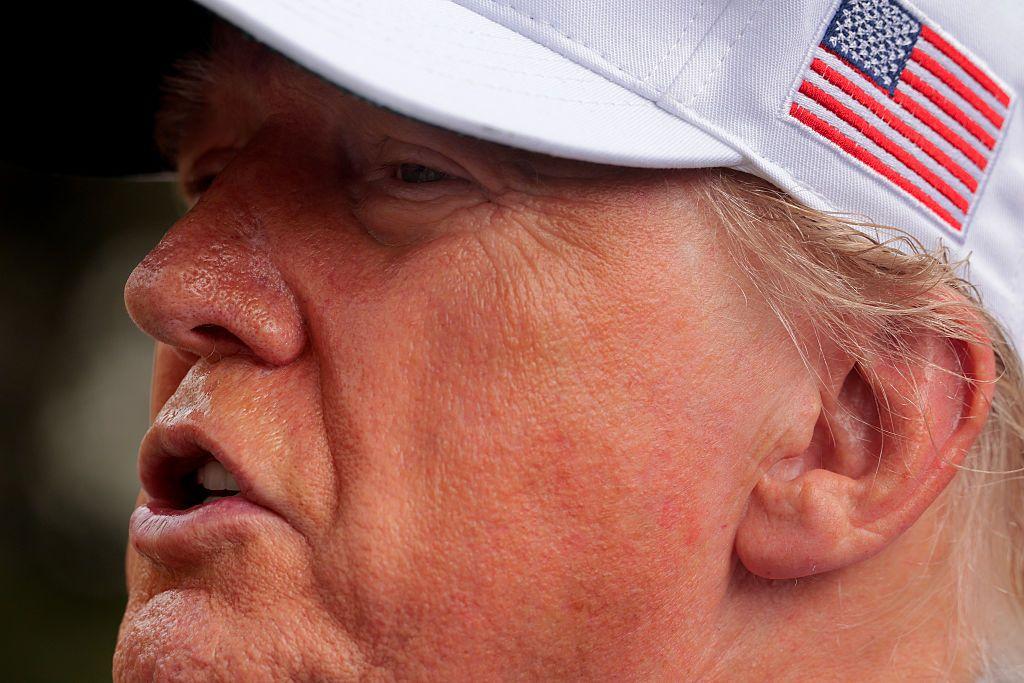 Donald Trump usando boné branco com a bandeira dos EUA estampada