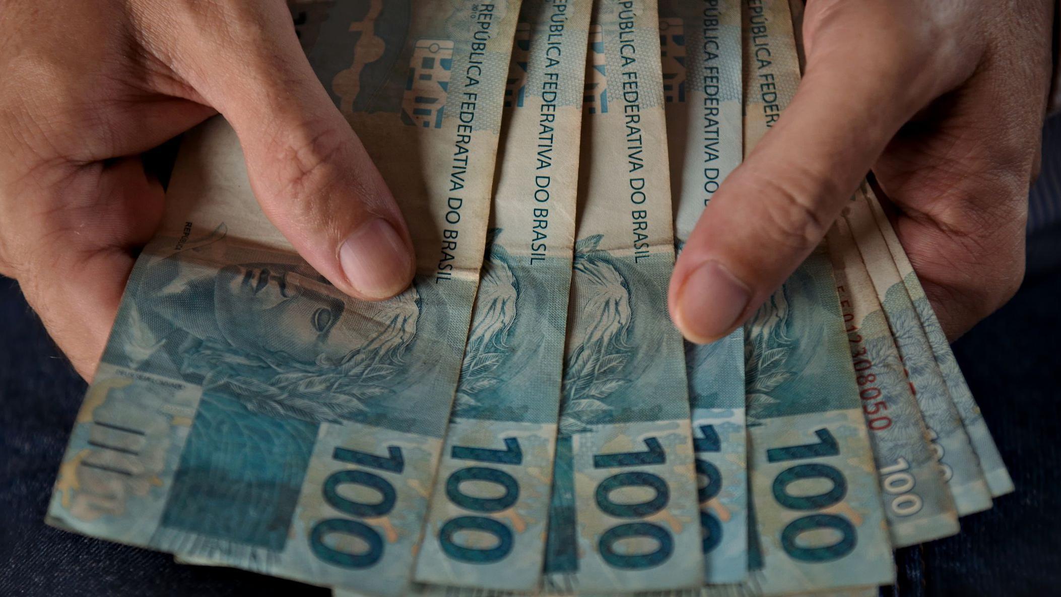 Mãos contando notas de cem reais