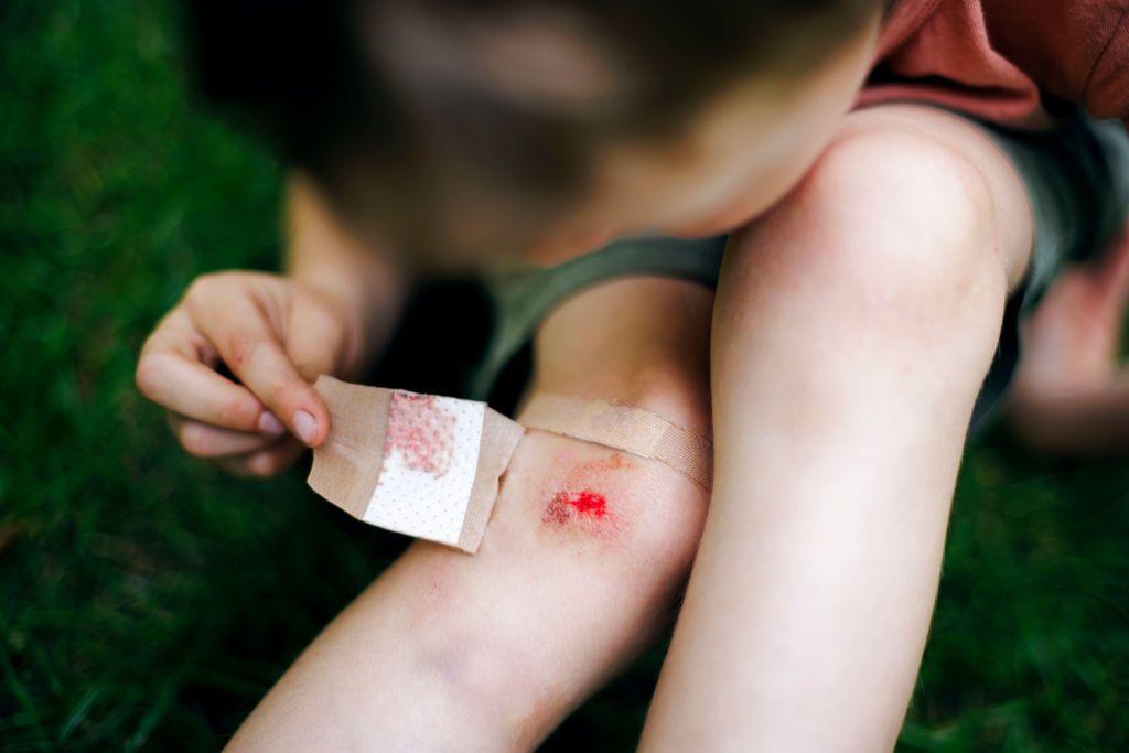 Un niño quitándose una venda de un corte sangrante en la rodilla.