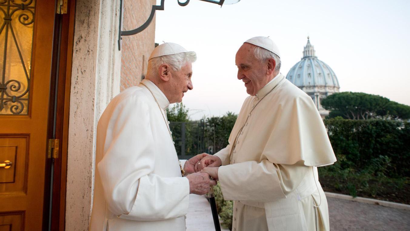 Papa Benedikt XVI (levo) i papa Franja (desno) se drž za ruke i gledaju jedan u drugog