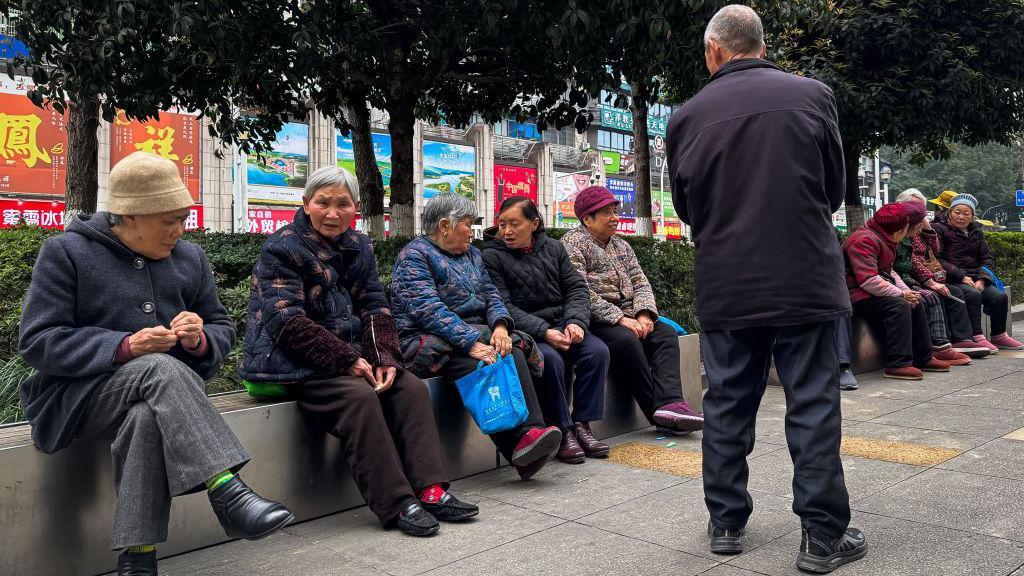 Grupo de idosos sentados em um banco público, conversando em uma área urbana de Chongqing, no sudoeste da China, em março de 2025