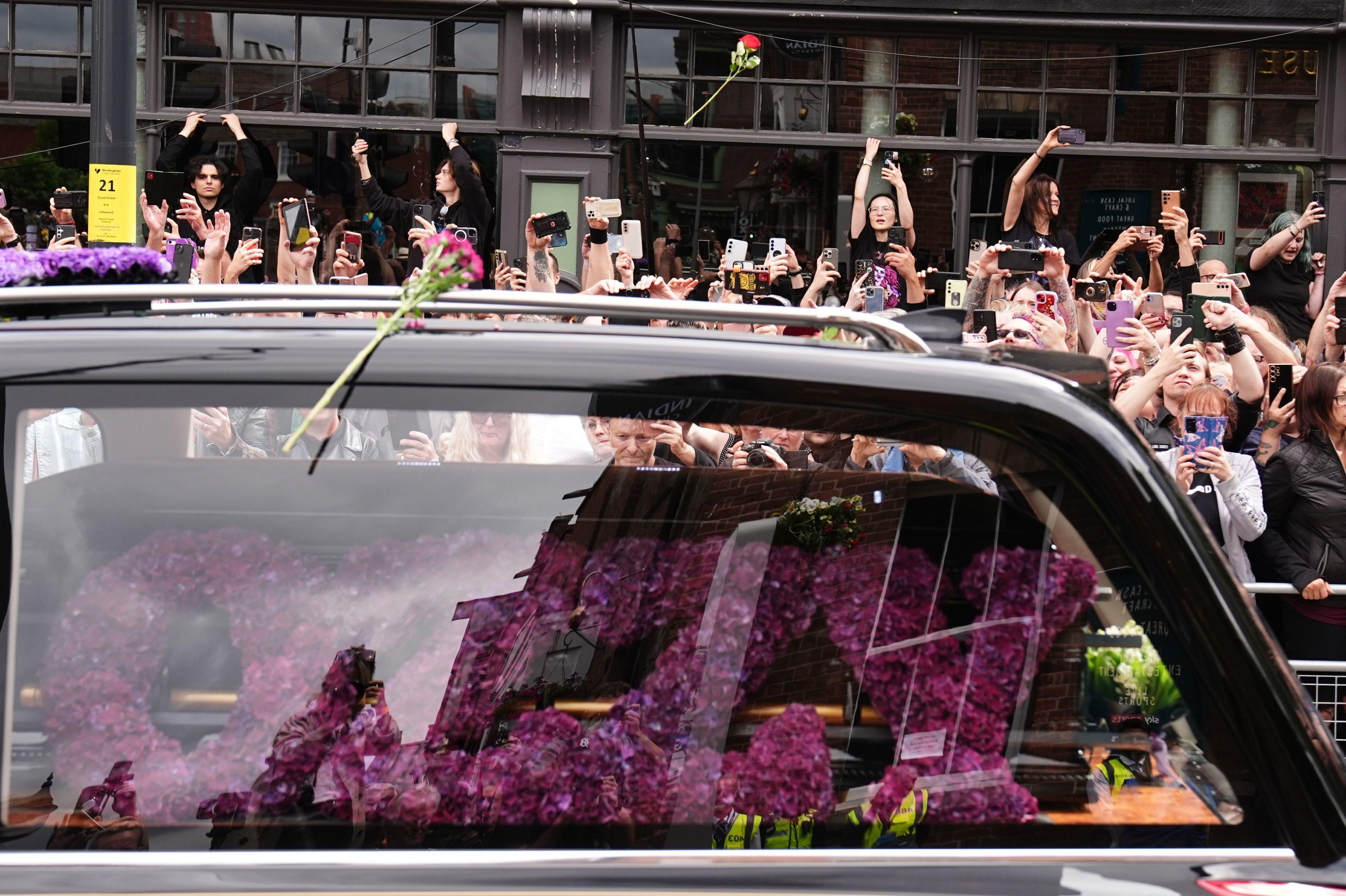 El carro fúnebre en el que transportaban el ataúd de Ozzy, mientras fanáticos les toman fotos.