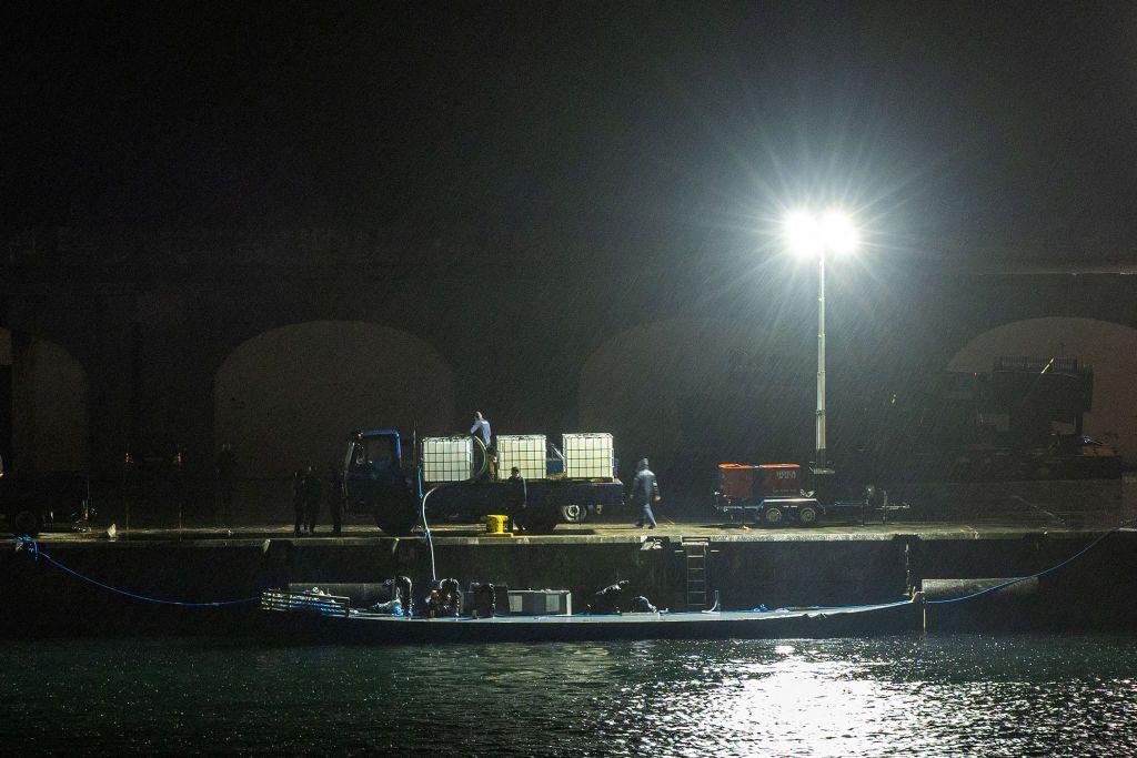Una imagen de noche de un sumergible en el agua mientras varias personas están descargándolo en un puerto de concreto.