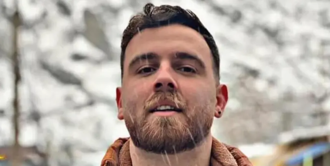 Imagem de comerciante de 26 anos, com cabelo curto e barba e uma roupa de frio, do pescoço pra cima