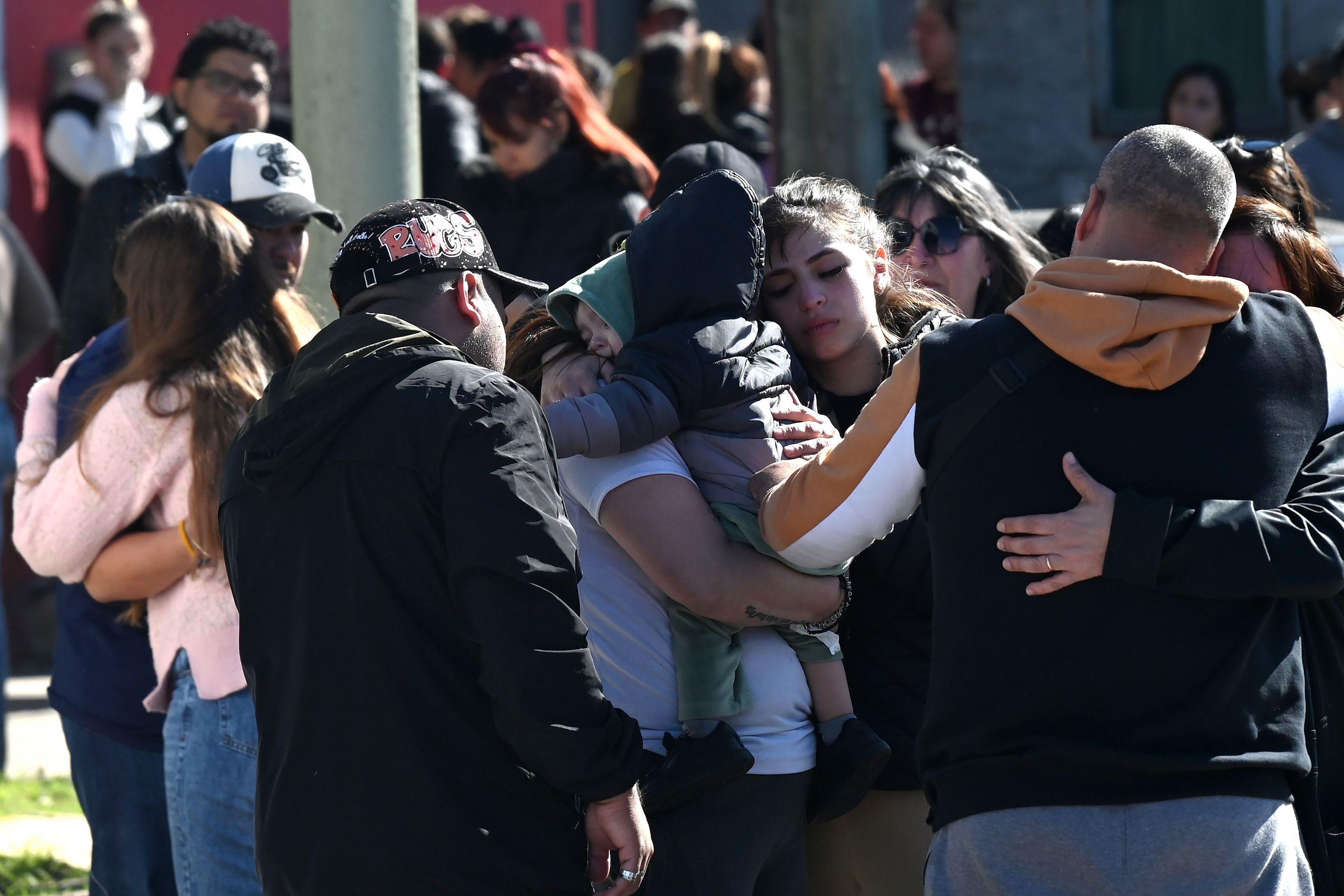Varias personas se abrazan compungidas. 