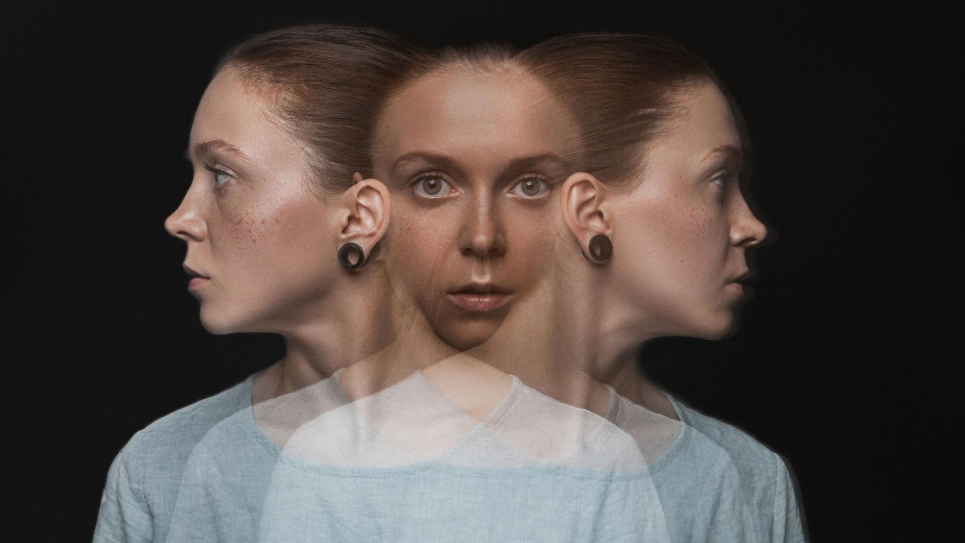 صورة لامرأة شابة ذات بشرة فاتحة وشعر مربوط إلى الخلف، تظهر بثلاثة وجوه متداخلة عبر تأثير بصري مزدوج. الوجه الأوسط ينظر مباشرة إلى الكاميرا بتعبير محايد، بينما الوجهان الجانبيان ينظران في اتجاهين متعاكسين (اليمين واليسار). ترتدي المرأة قميصاً قطنياً أزرق فاتح، والخلفية سوداء بالكامل.