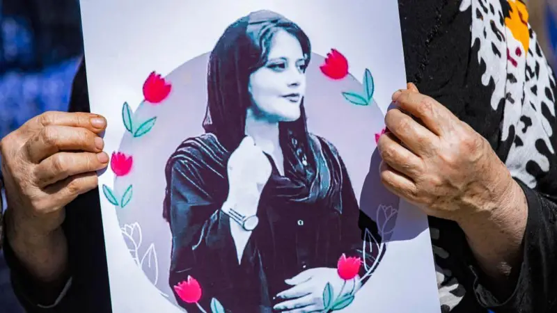 Seorang demonstran memegang poster Mahsa Amini, perempuan muda yang diduga meninggal dalam tahana polisi syariah. Kematiannya telah memicu gelombang besar demonstrasi di Iran.