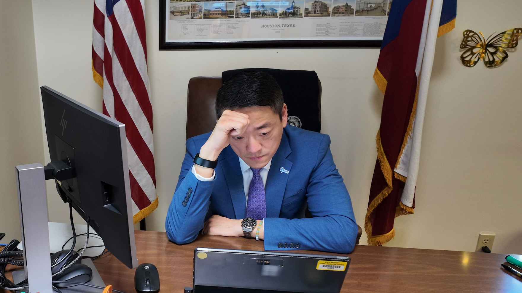Gene Wu sentado en su escritorio de oficina, mirando un dispositivo frente a él.
