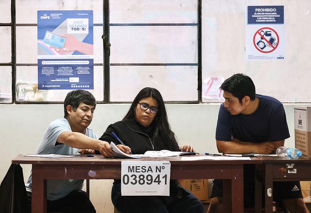 Tres personas tras una mesa electoral en un centro de votación de Lima. 