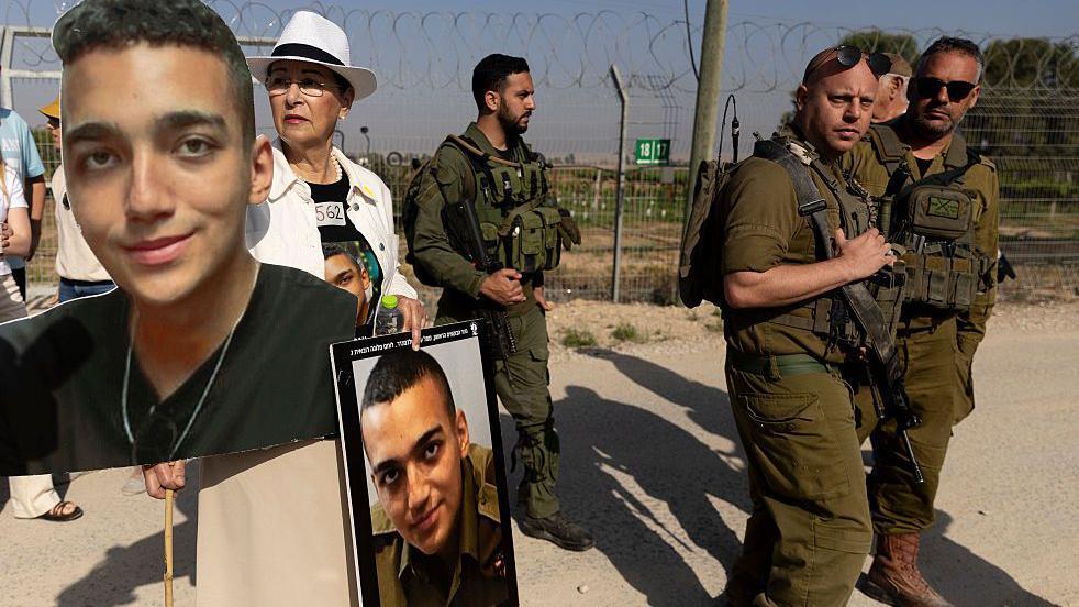 Varda Ben Baruch sostiene fotos de su nieto, el rehén israelí-estadounidense Edan Alexander, mientras camina cerca de soldados israelíes durante una concentración de familiares de rehenes retenidos en la Franja de Gaza, en Nir Oz, cerca de la frontera con la Franja de Gaza, el 20 de abril de 2025 en Nir Oz, Israel.