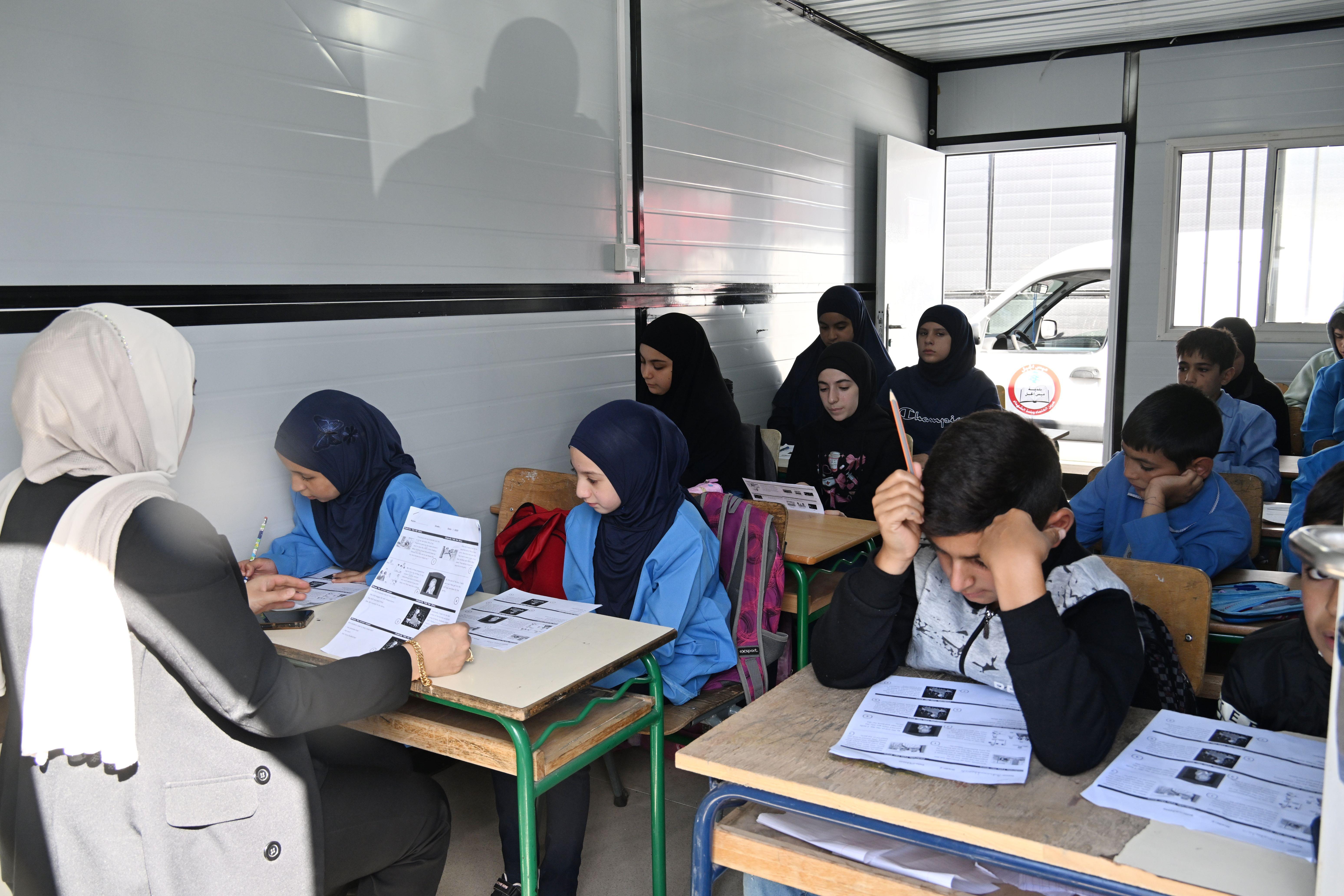تلاميذ من بلدية ميس الجبل يحضرون دروسهم في صفوف مؤقتة داخل حاويات في منطقة مرجعيون جنوب لبنان، بعدما تضررت مدارسهم جراء الهجمات الإسرائيلية قرب الحدود، في 20 أكتوبر/تشرين الأول 2025.