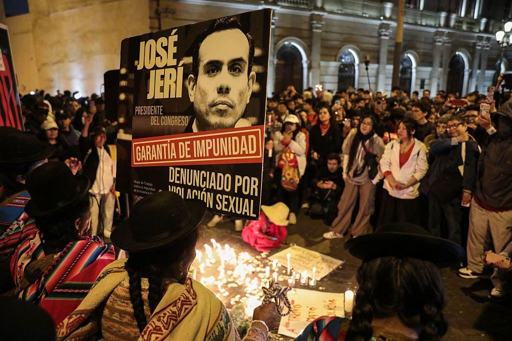 Multitud con una pancarta y rodeando un grupo de velas en el suelo.
