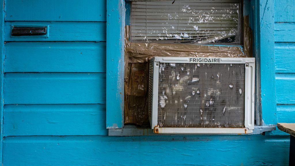 Aparelho de ar-condicionado instalado na janela de uma casa de madeira pintada de azul