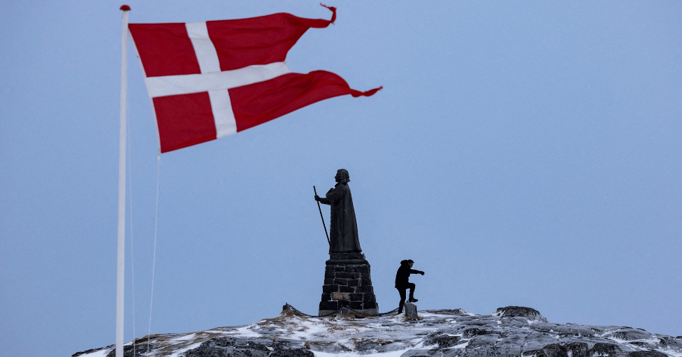 Una estatua sobre un monumento cubierto por el hielo en Nuuk, Groenlandia. Sobre ella ondea la bandera de Dinamarca. 