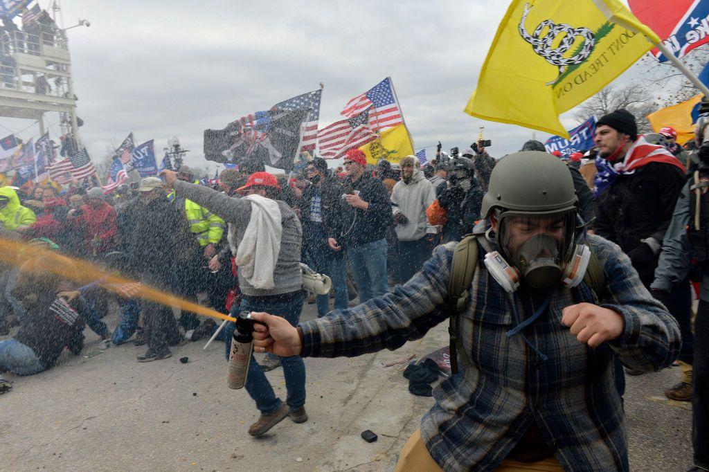 Un manifestante libera un gas en medio de una manifestación mientras lleva puesta una máscara de gas. En el fondo, se ven decenas de personas conmocionadas, algunas en el piso, otras ondeando banderas.