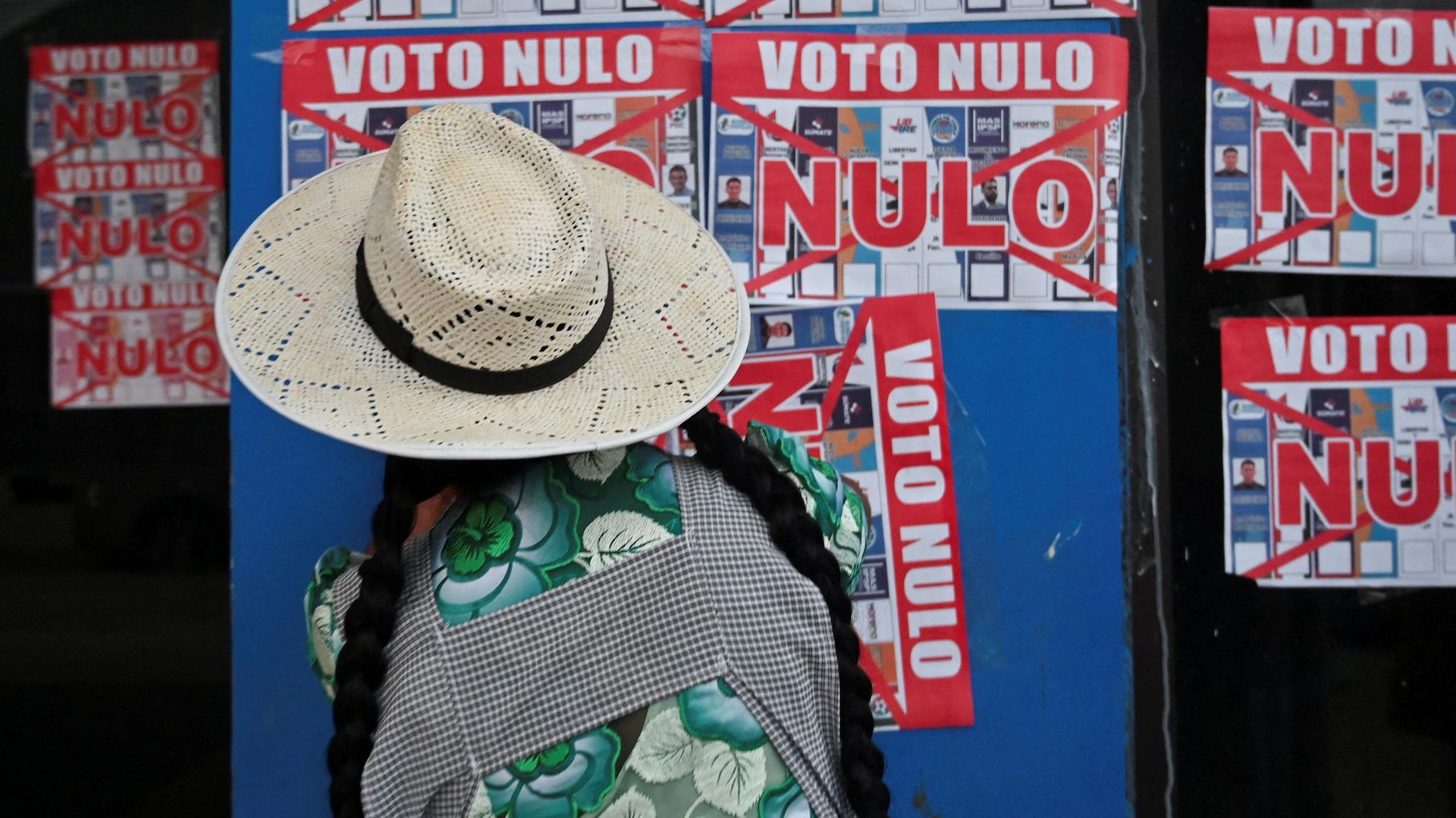 Una mujer pega un cartel que dice "Voto Nulo" en la pared exterior de una casa de campaña antes de las elecciones generales de Bolivia, en Chapare, Bolivia, el 2 de agosto de 2025.