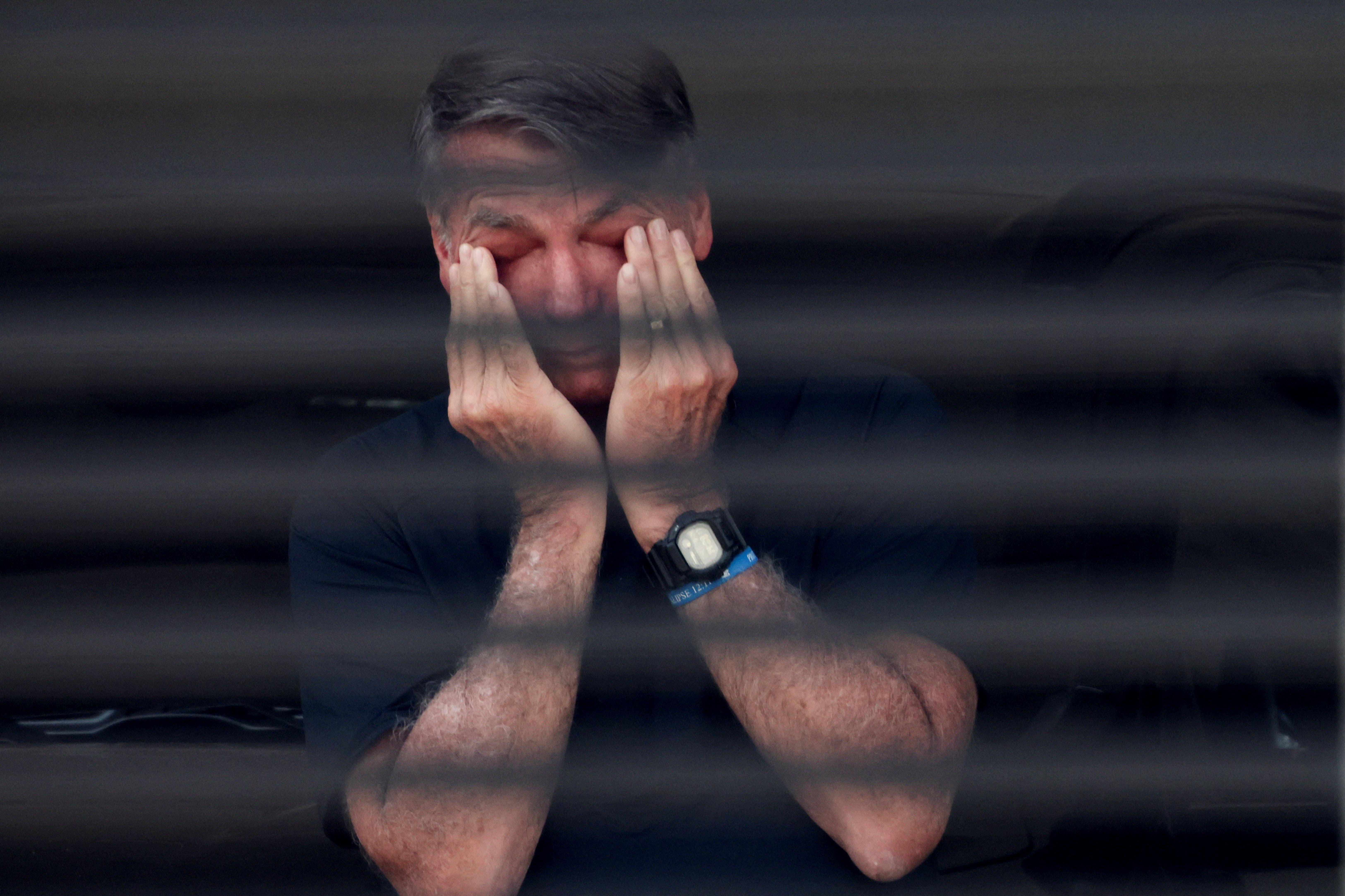 Bolsonaro leva as mãos ao rosto, atrás da grade de sua casa