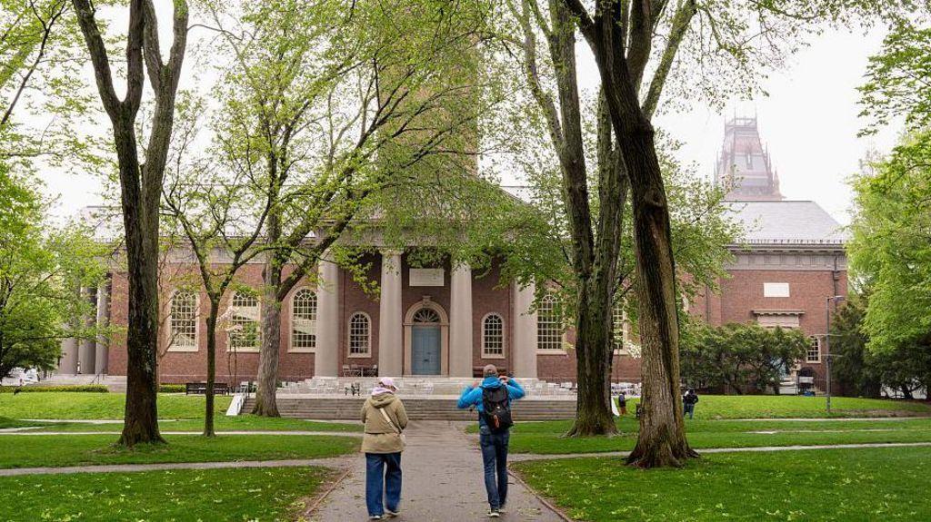 Dos personas caminan con la fachada de la Universidad de Harvard al fondo