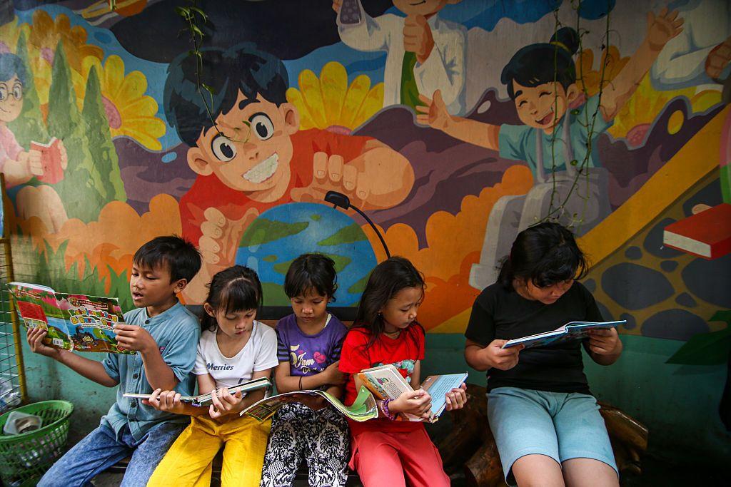 Cinco crian&ccedil;as, uma ao lado da outra, lendo livros