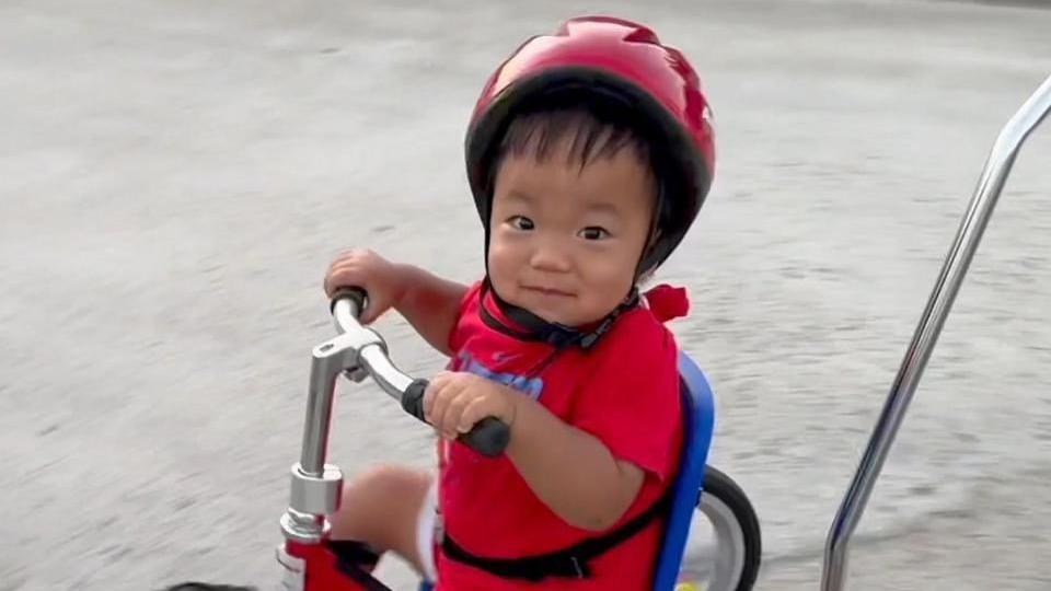 Oliver Chu en un triciclo rojo con casco y mirando a la cámara.