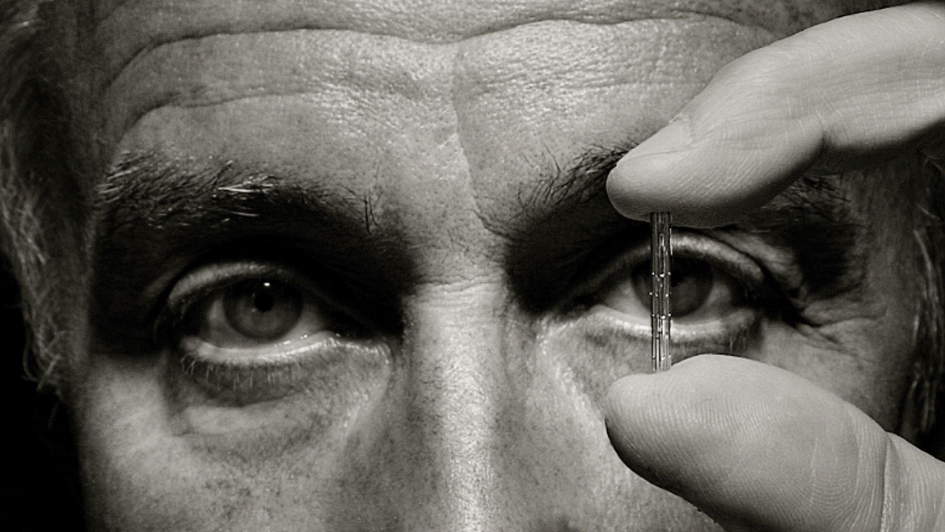 Julio Palmaz en fotografía blanco y negro, primer plano, sólo ojos y sus dedos sosteniendo un stent.