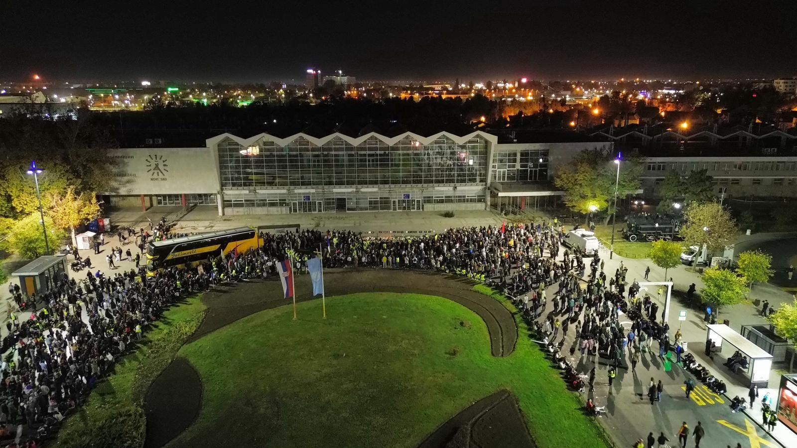 Snimak iz ptičije perspektive gde se vide ljudi dok stoje ispred Železničke stanice u Novom Sadu