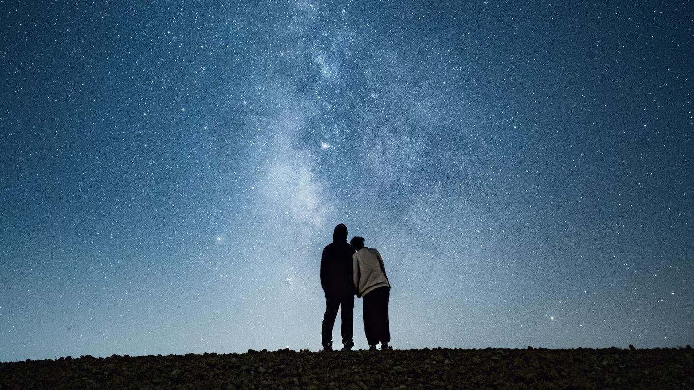 Pareja abrazada mirando las estrellas en la noche.