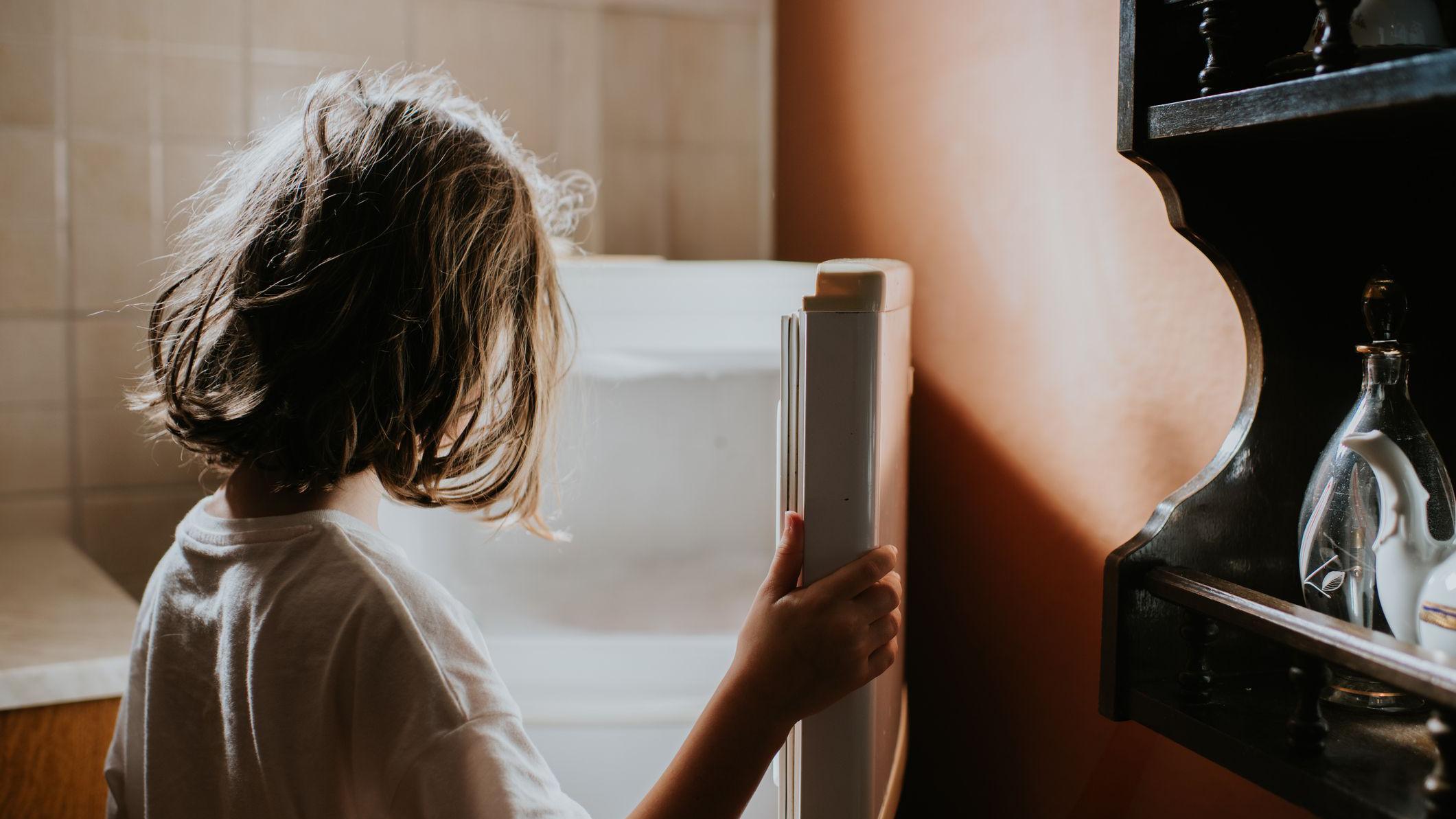 Una niña de espaldas abre una nevera vacía. 